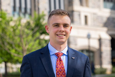 Portrait of Thomas Feely standing outside in a suit, with a Virginia Tech tie and pin.